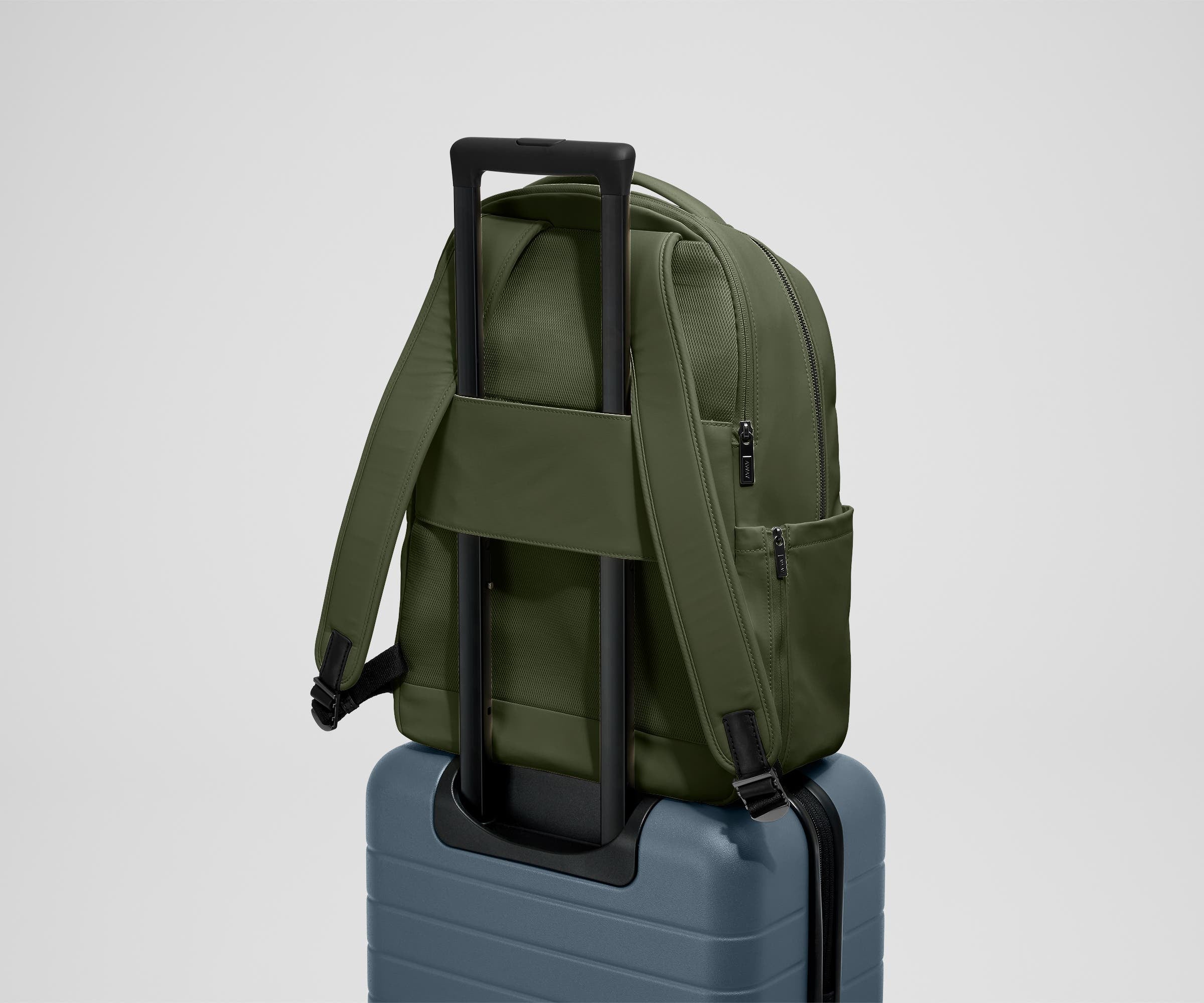 The Commuter Backpack on top of an Away suitcase, attached by the trolley pass-through sleeve
