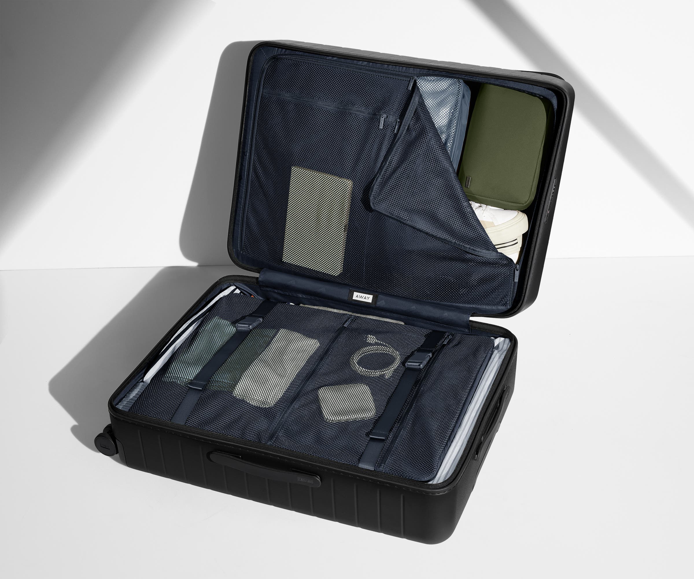 The Large suitcase in Jet Black shown open on its side and packed with Away's packing organizers to show capacity and the interior compression system, designed to help you pack more in