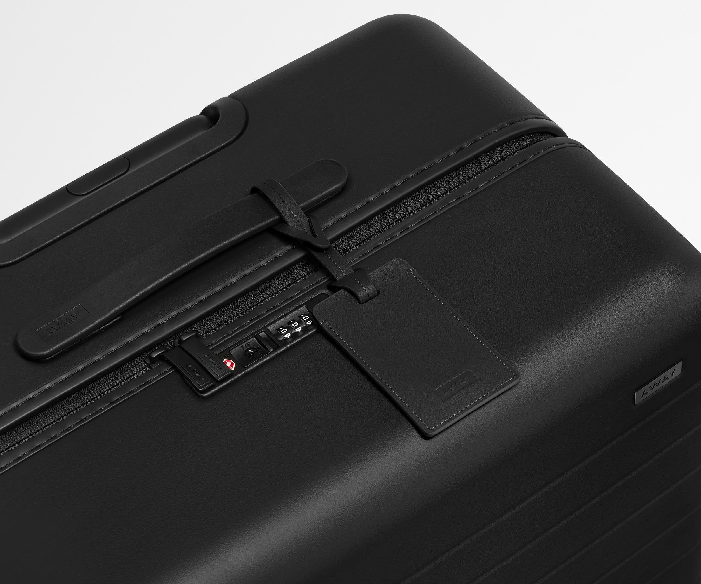 The Large suitcase in Jet Black shown shown from above highlighting TSA-approved combination lock and recycled leather luggage tag