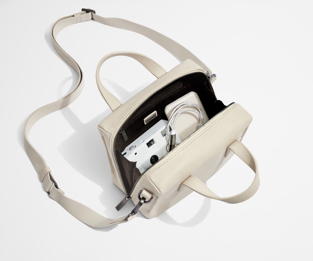 Main interior packed with a camera, charging cord, and portable charger. Shown with the removable shoulder strap