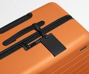 The Large suitcase in Sorbet Orange shown shown from above highlighting TSA-approved combination lock and recycled leather luggage tag