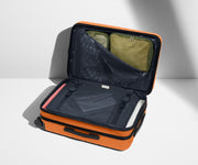 The Bigger Carry-On Flex suitcase in Sorbet Orange shown open on its side and packed with Away's packing organizers to show capacity and the interior compression system, designed to help you pack more in