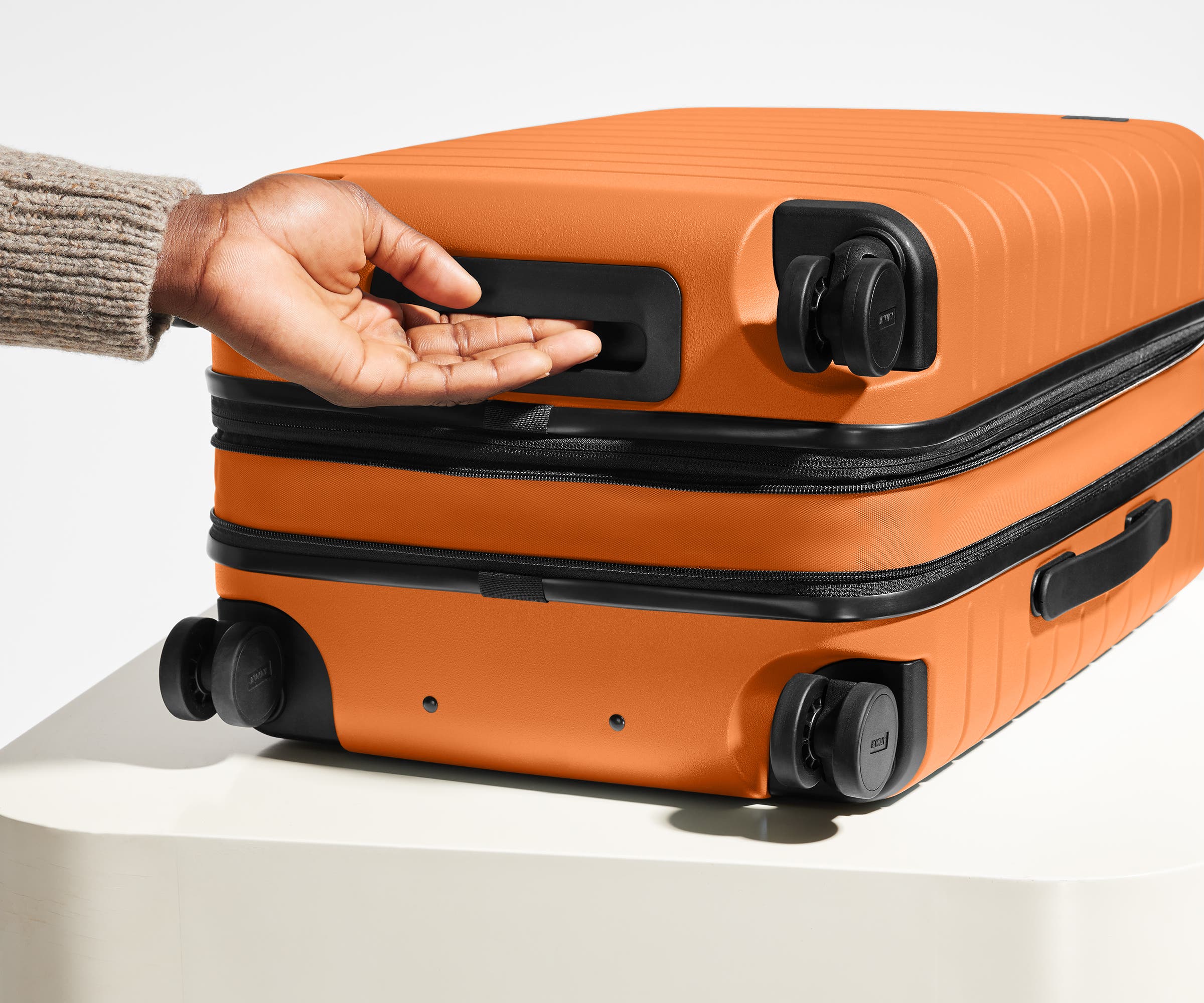 The Bigger Carry-On Flex suitcase in Sorbet Orange shown from below highlighting the underside grab handle