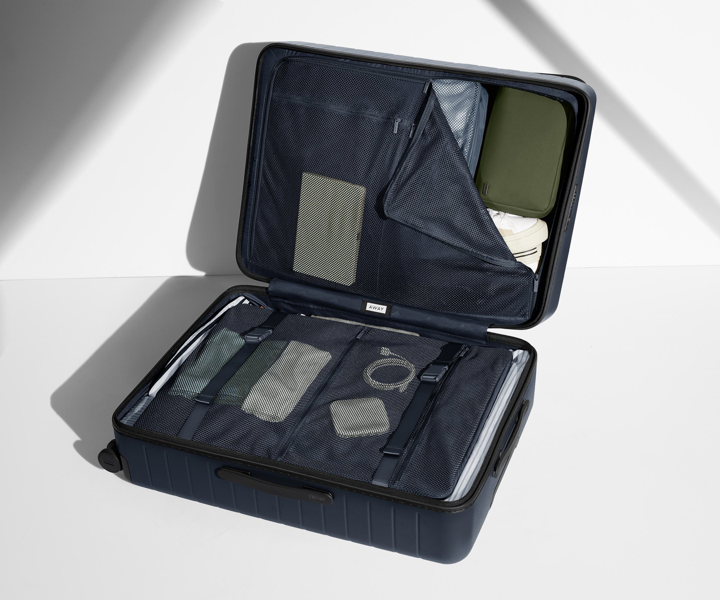 The Large suitcase in Navy Blue shown open on its side and packed with Away's packing organizers to show capacity and the interior compression system, designed to help you pack more in