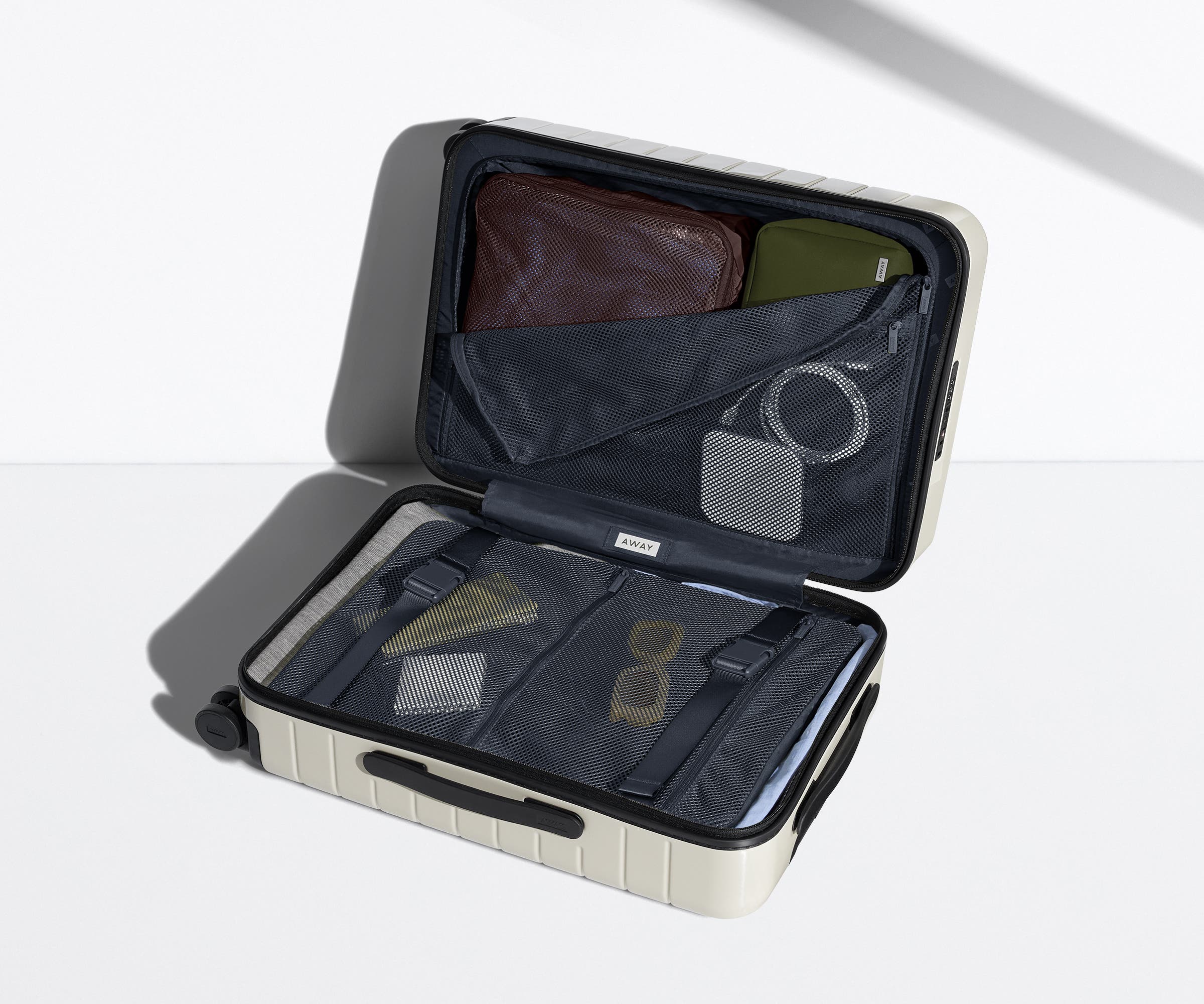 The Bigger Carry-On suitcase in Salt White (Gloss) shown open on its side and packed with Away's packing organizers to show capacity and the interior compression system, designed to help you pack more in