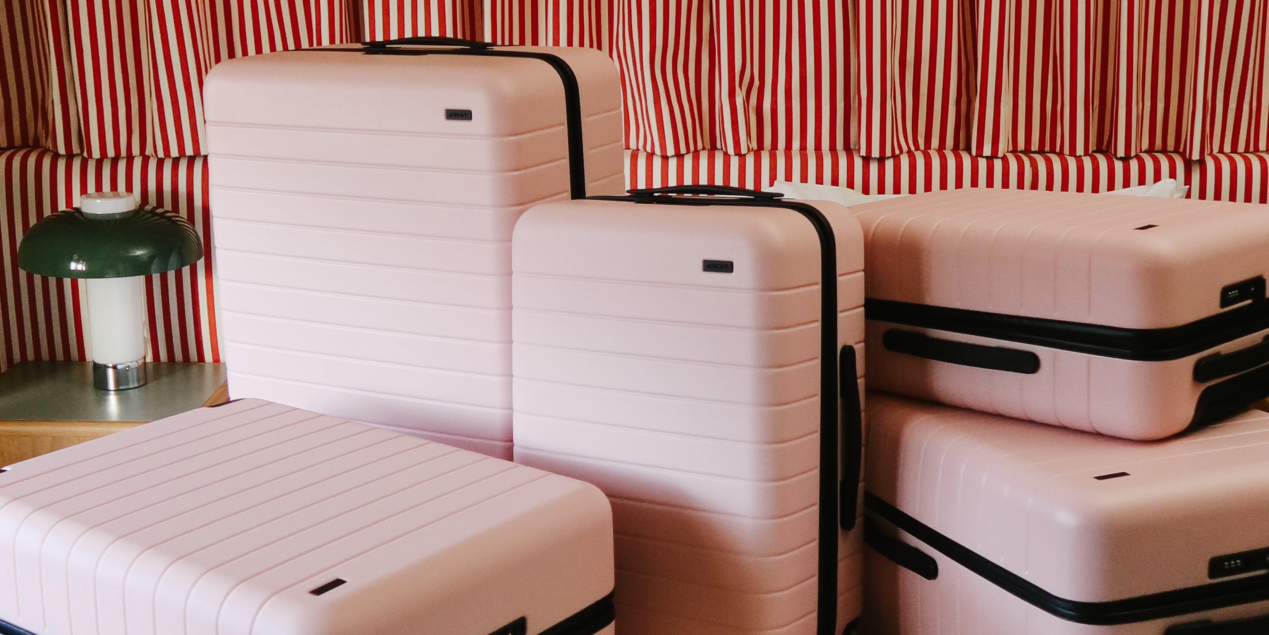 Set of pink suitcases with black handles against a red and white striped background