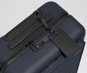 The Front Pocket Carry-On suitcase in Navy Blue shown shown from above highlighting TSA-approved combination lock and black leather luggage tag