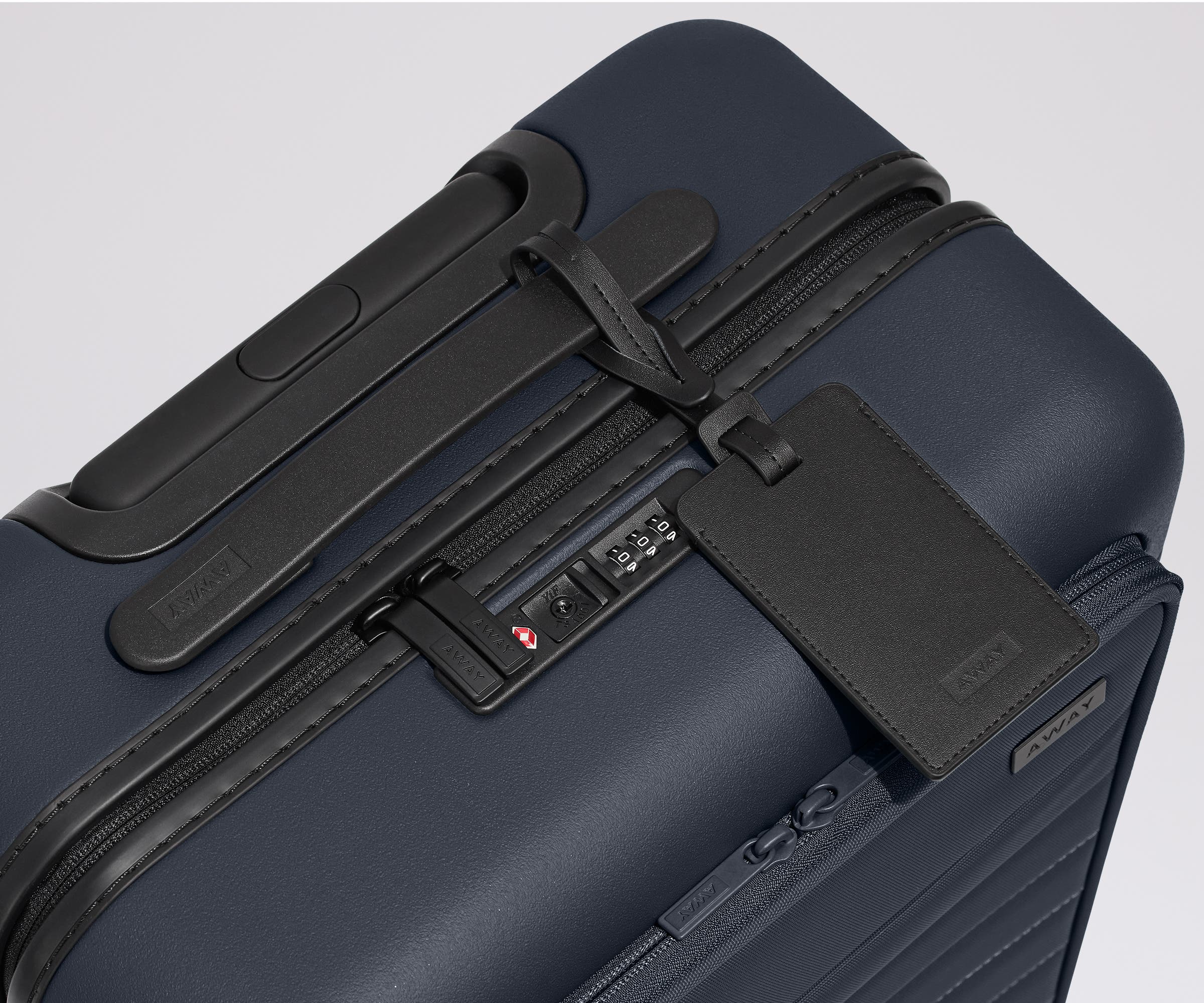 The Front Pocket Carry-On suitcase in Navy Blue shown shown from above highlighting TSA-approved combination lock and black leather luggage tag