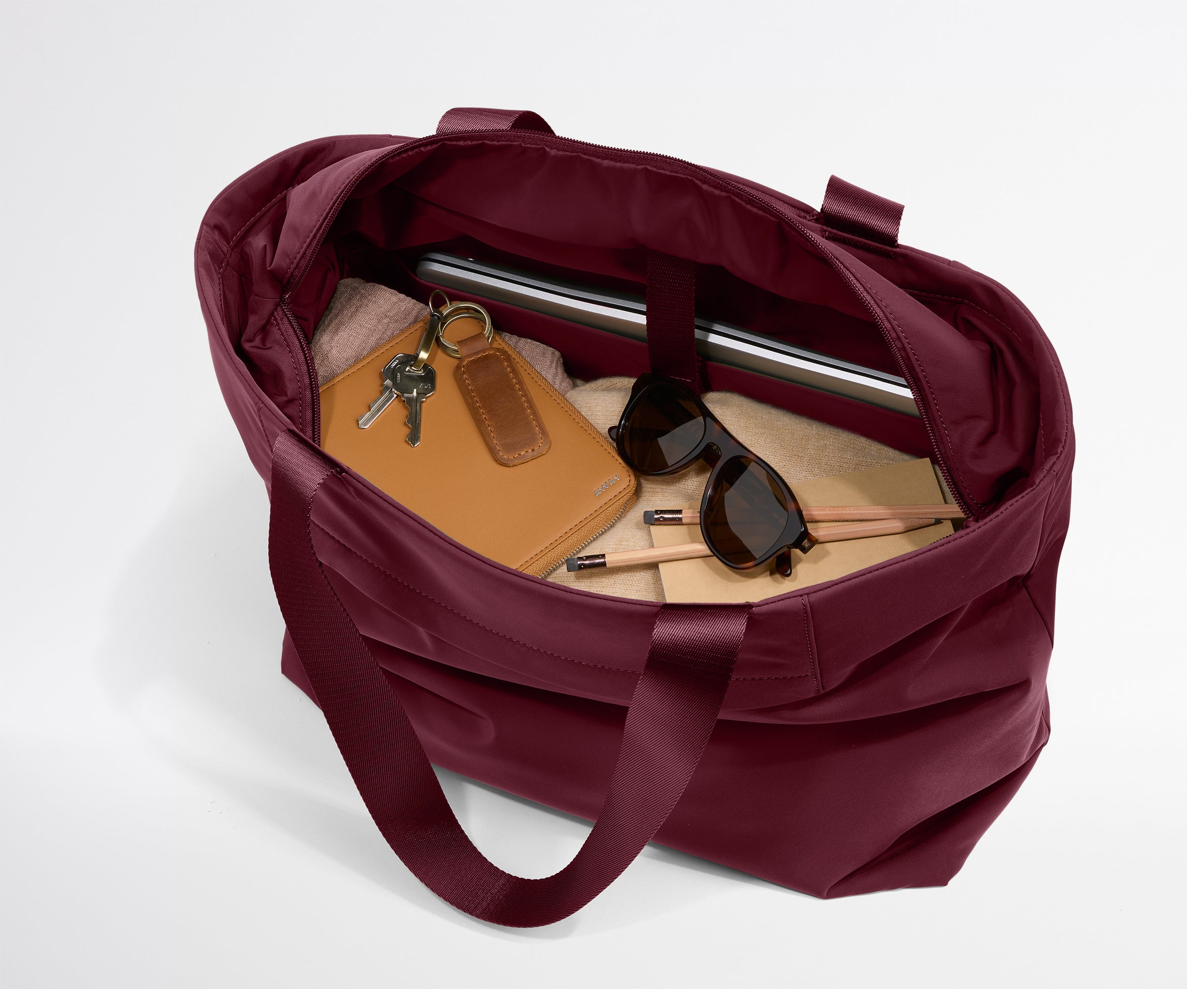 Maroon tote bag with items like a notebook, keys, and sunglasses on a light gray background