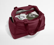 Maroon duffel bag with items inside on a white background