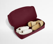 Maroon weekender with a shoe organizer with white and beige shoes on a light gray background