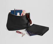 Black pouch with sunglasses, passport, and other items on a light gray background