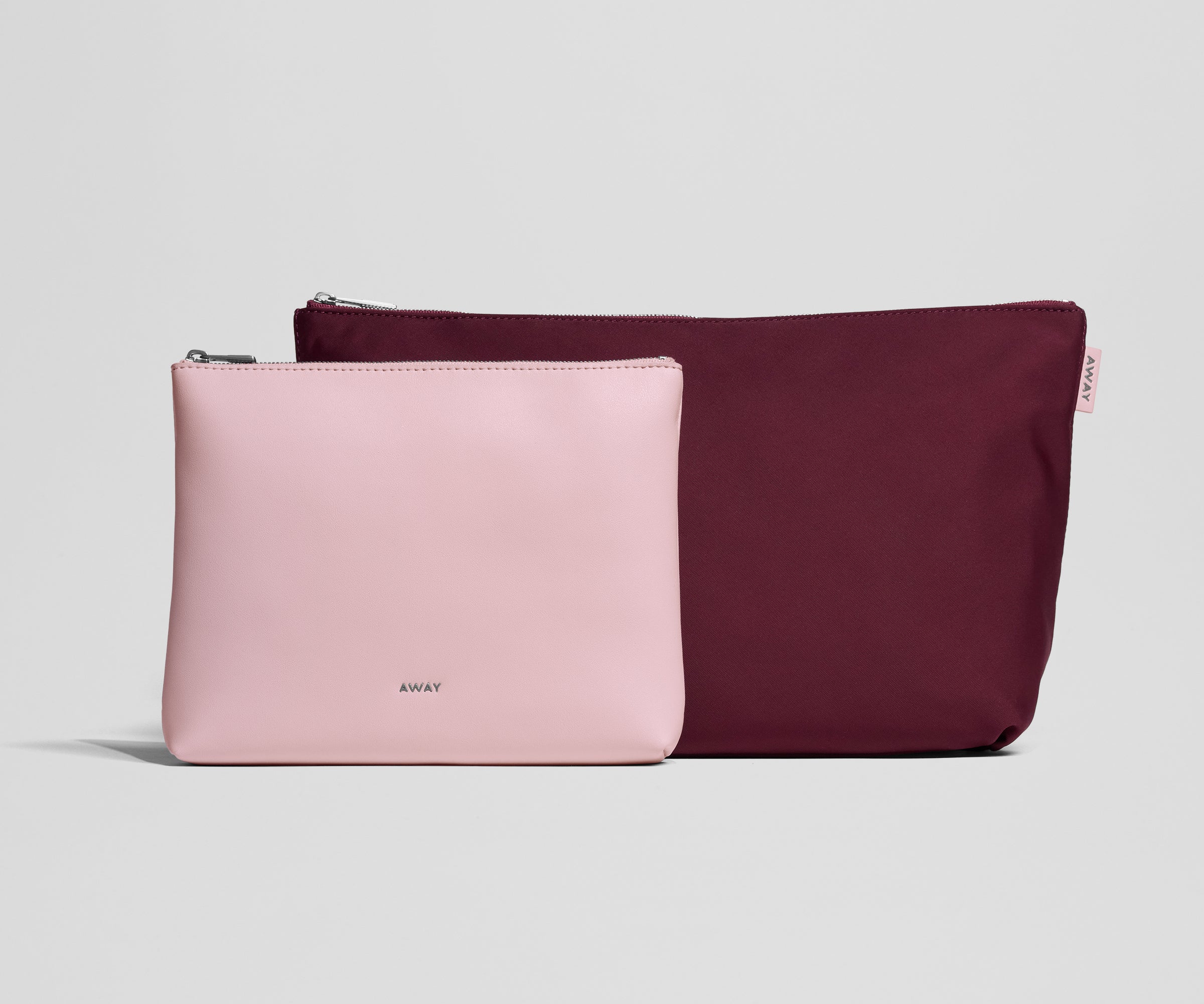 Pink and burgundy travel pouches with 'AWAY' branding on a light gray background