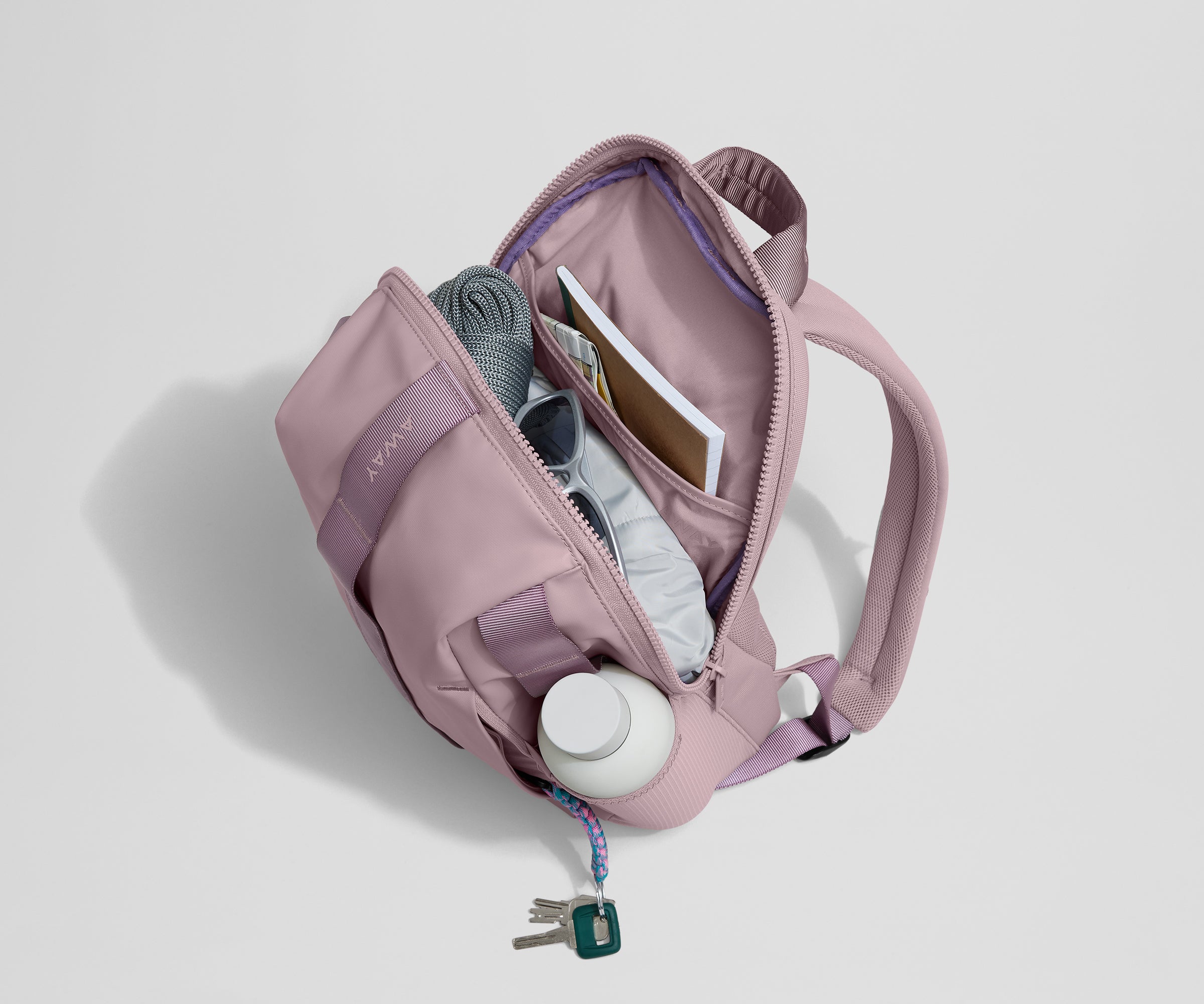 Daypack packed with a light jacket, sunglasses, notebook, map, and other travel gear. Water bottle featured in the exterior water bottle pocket.