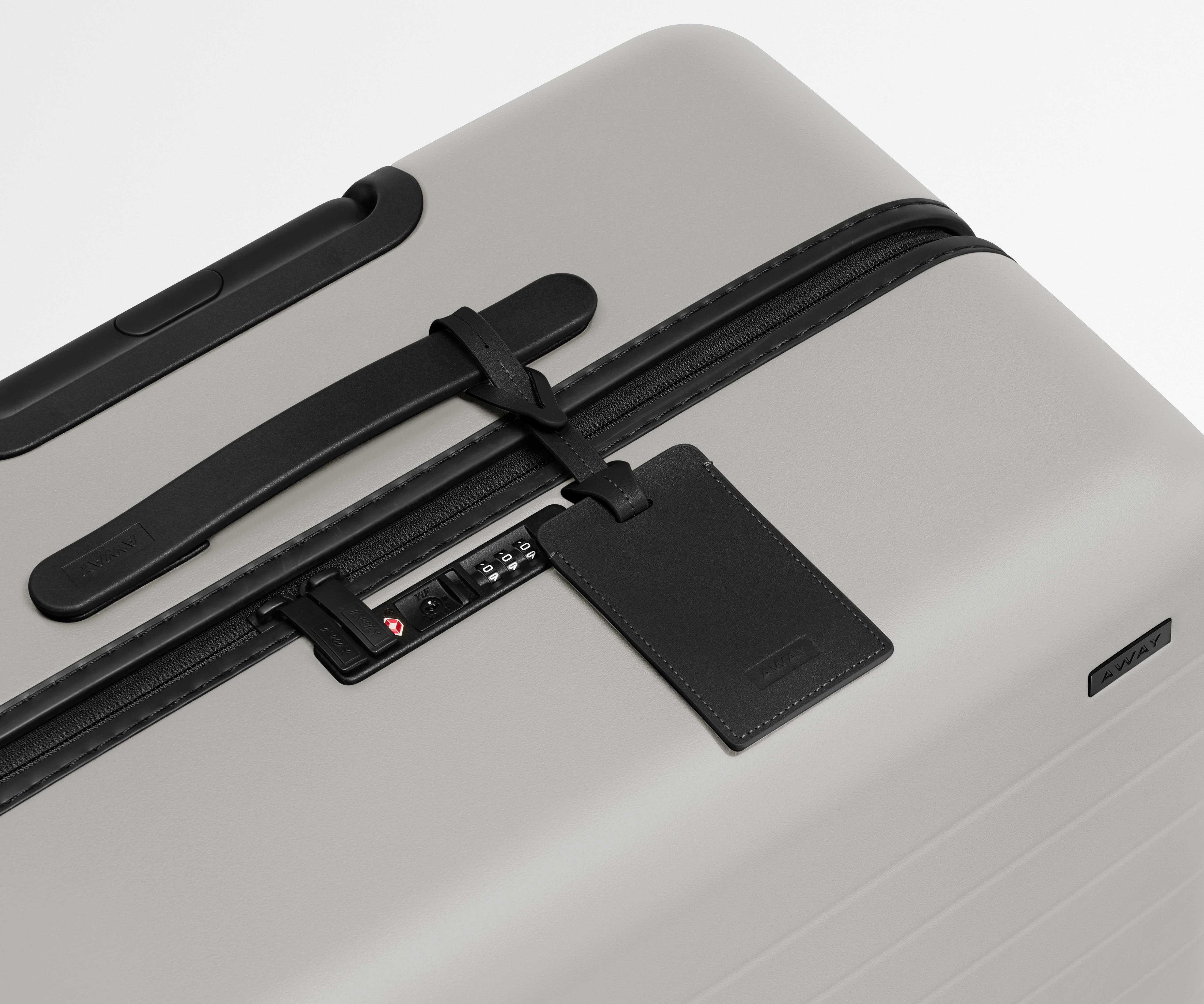 The Large suitcase in Cloud Gray shown shown from above highlighting TSA-approved combination lock and recycled leather luggage tag