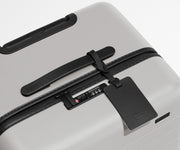 The Trunk suitcase in Cloud Gray shown shown from above highlighting TSA-approved combination lock and recycled leather luggage tag