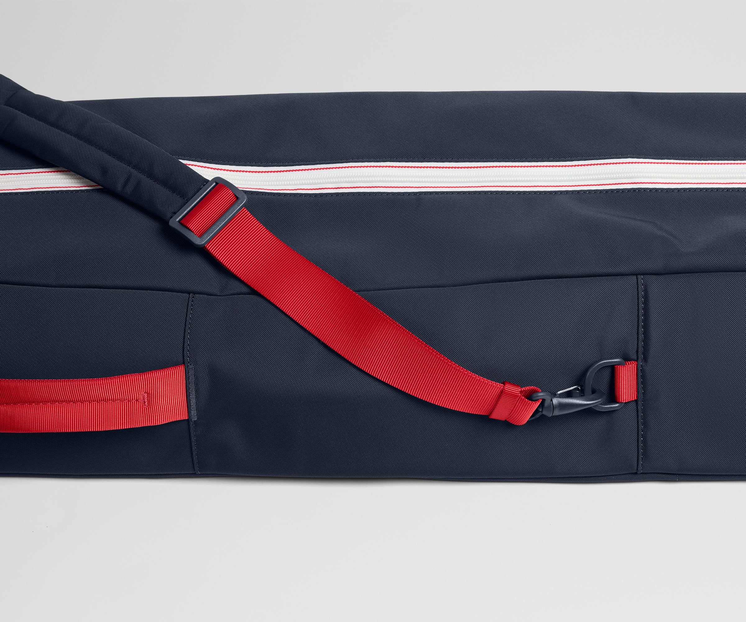 Navy bag with red strap and zipper on a light gray background