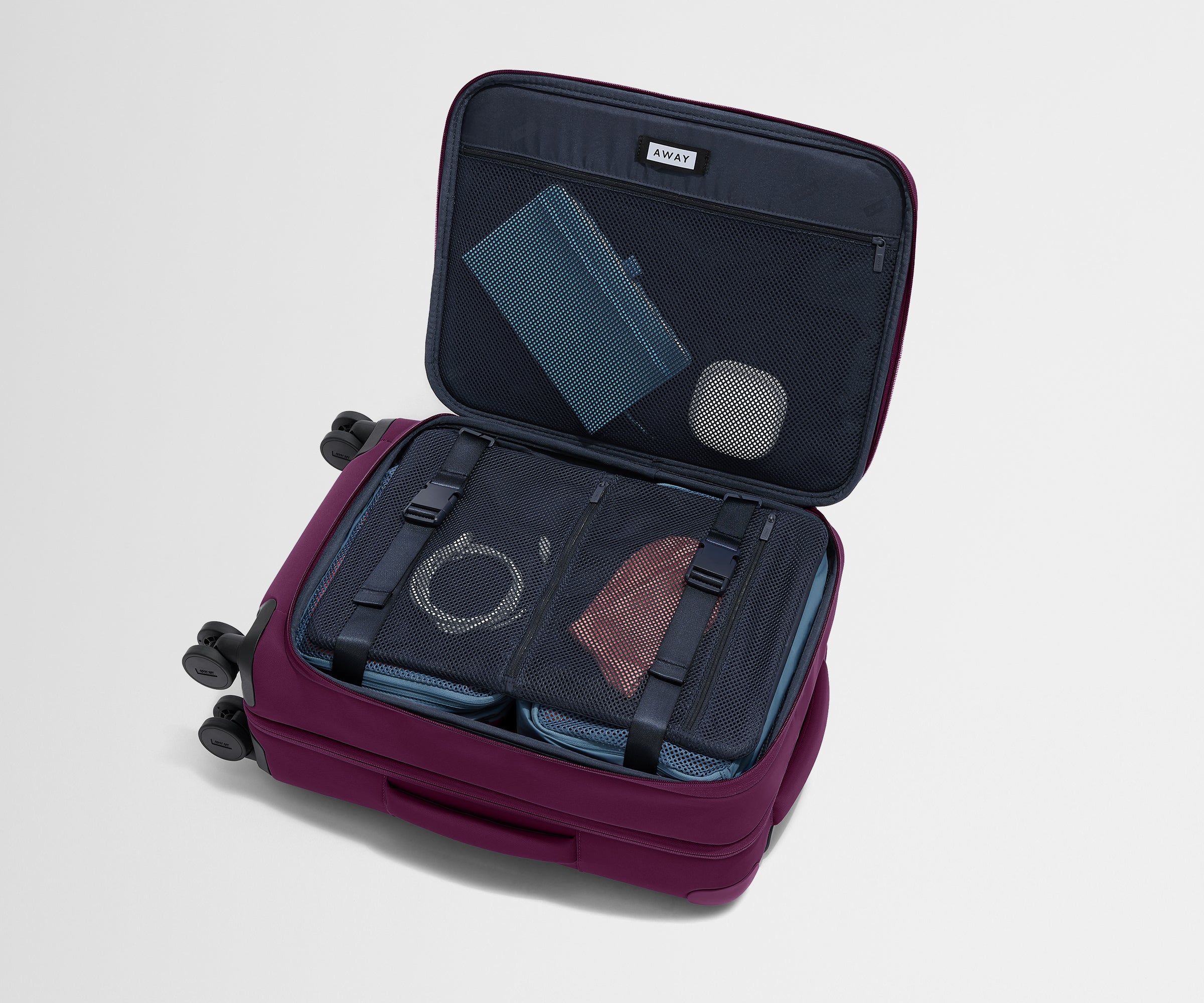 The Softside Carry-On suitcase in Coast Blue shown open on its side and packed with Away's packing organizers to show capacity and the interior compression system, designed to help you pack more in