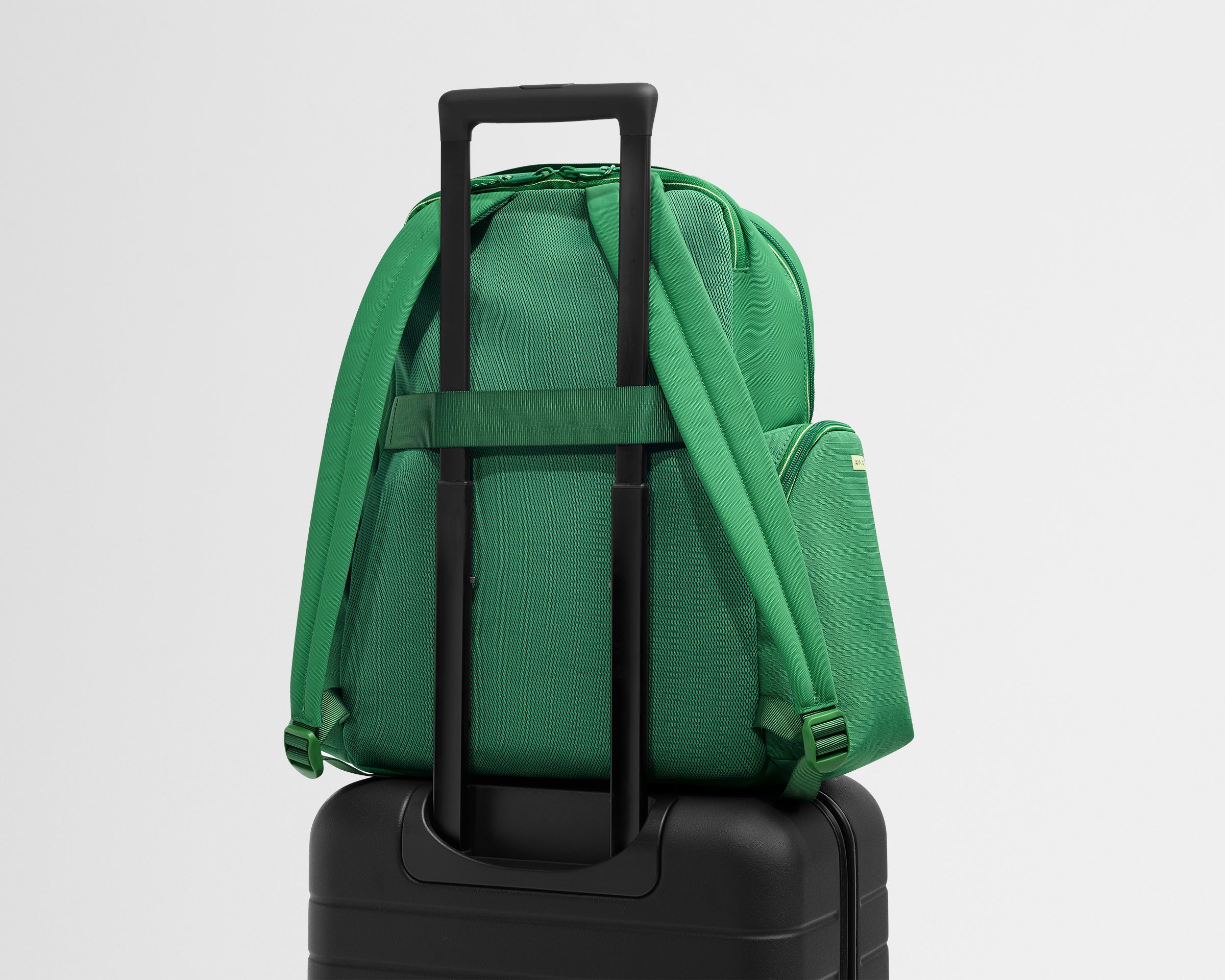 Green backpack attached to a black suitcase on a light gray background