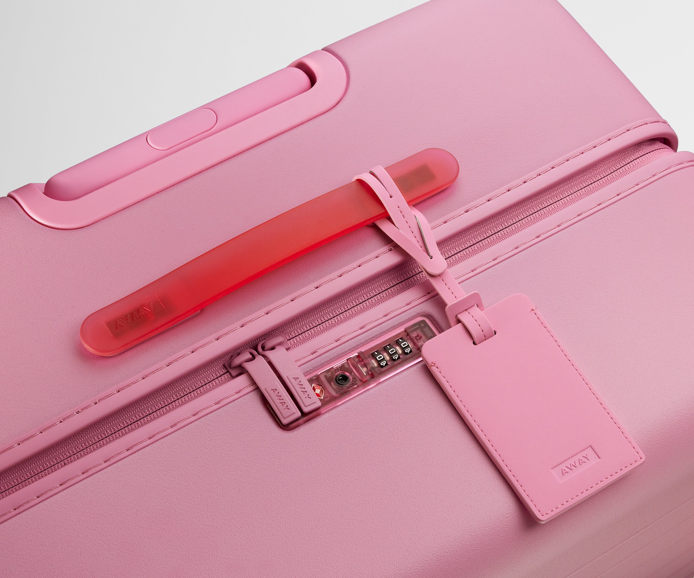The Large suitcase in Hot Pink shown shown from above highlighting TSA-approved combination lock and recycled leather luggage tag