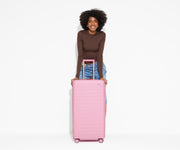A 5'9" model is posing and leaning on The Trunk suitcase in Hot Pink with the handle raised to show size and scale