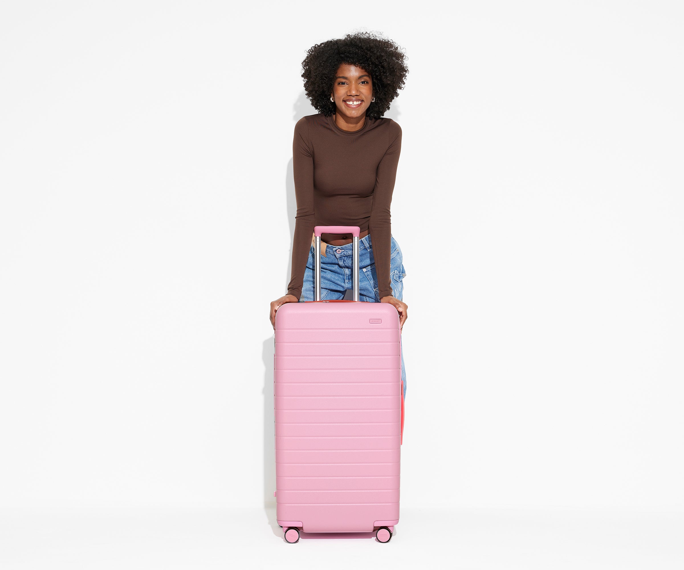 A 5'9" model is posing and leaning on The Trunk suitcase in Hot Pink with the handle raised to show size and scale