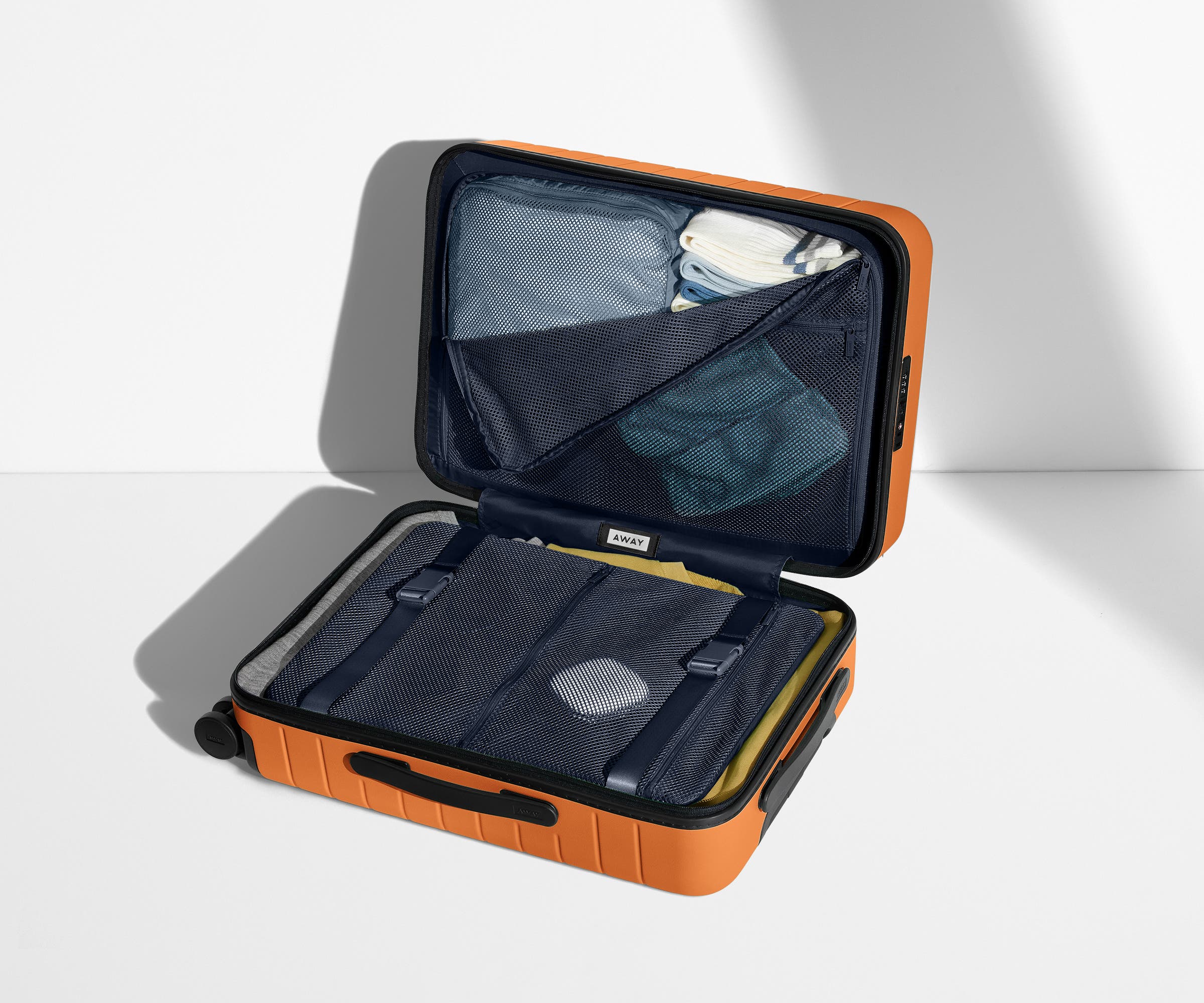 The Bigger Carry-On suitcase in Sorbet Orange shown open on its side and packed with Away's packing organizers to show capacity and the interior compression system, designed to help you pack more in