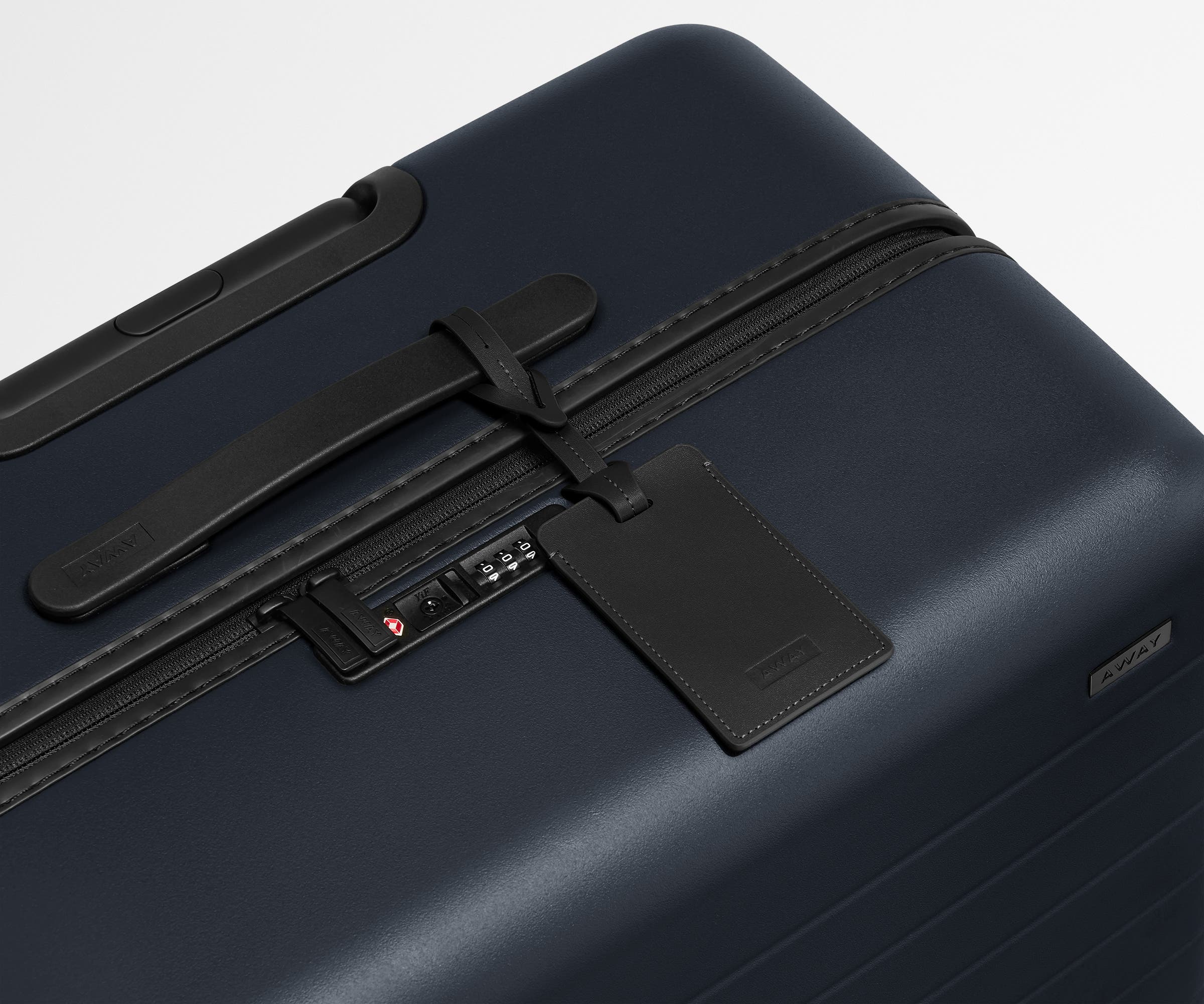 The Large suitcase in Navy Blue shown shown from above highlighting TSA-approved combination lock and recycled leather luggage tag
