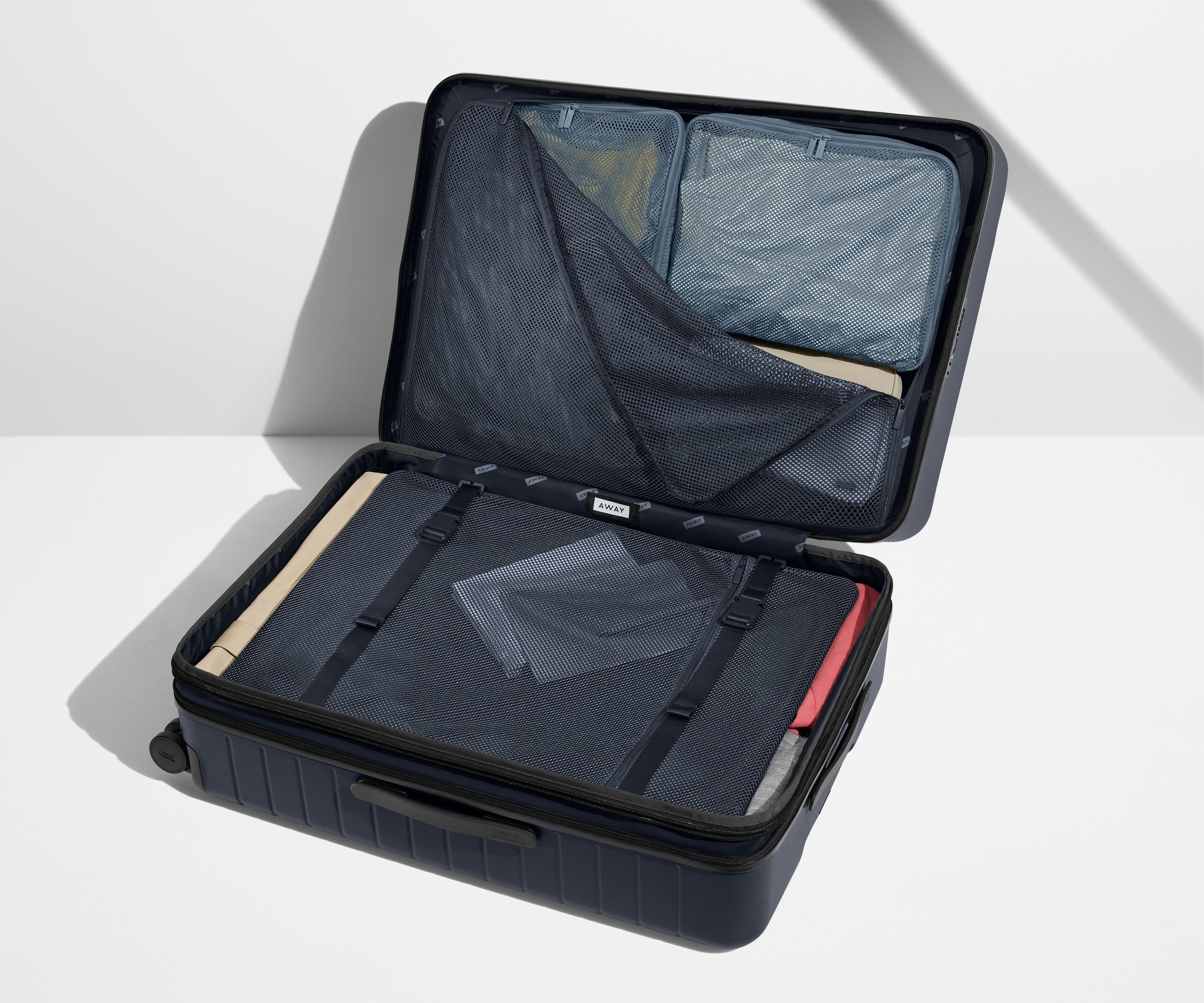 The Large Flex suitcase in Navy Blue shown open on its side and packed with Away's packing organizers to show capacity and the interior compression system, designed to help you pack more in