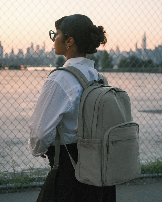 Person wearing a light gray backpack with a city skyline in the background