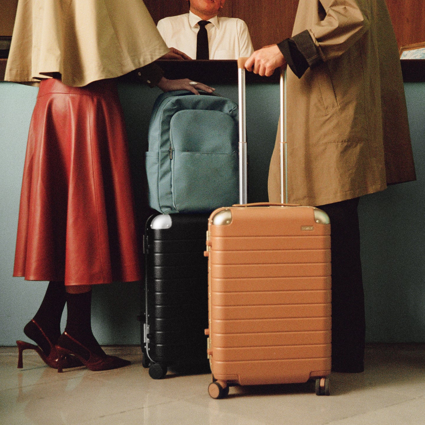 Two suitcases, one brown and one black, with a person holding a blue backpack in the background.