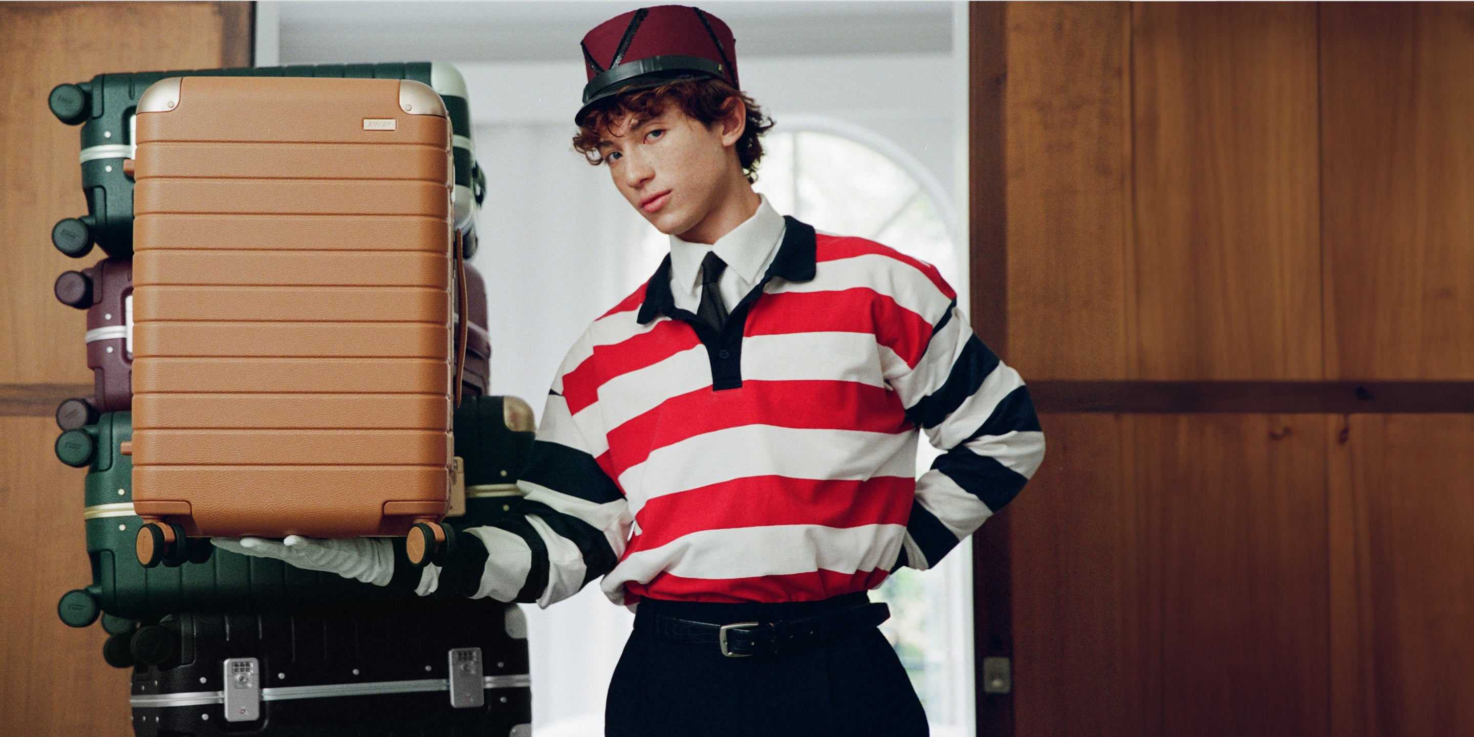 Person in a striped sweater holding a suitcase with another suitcase in the background.