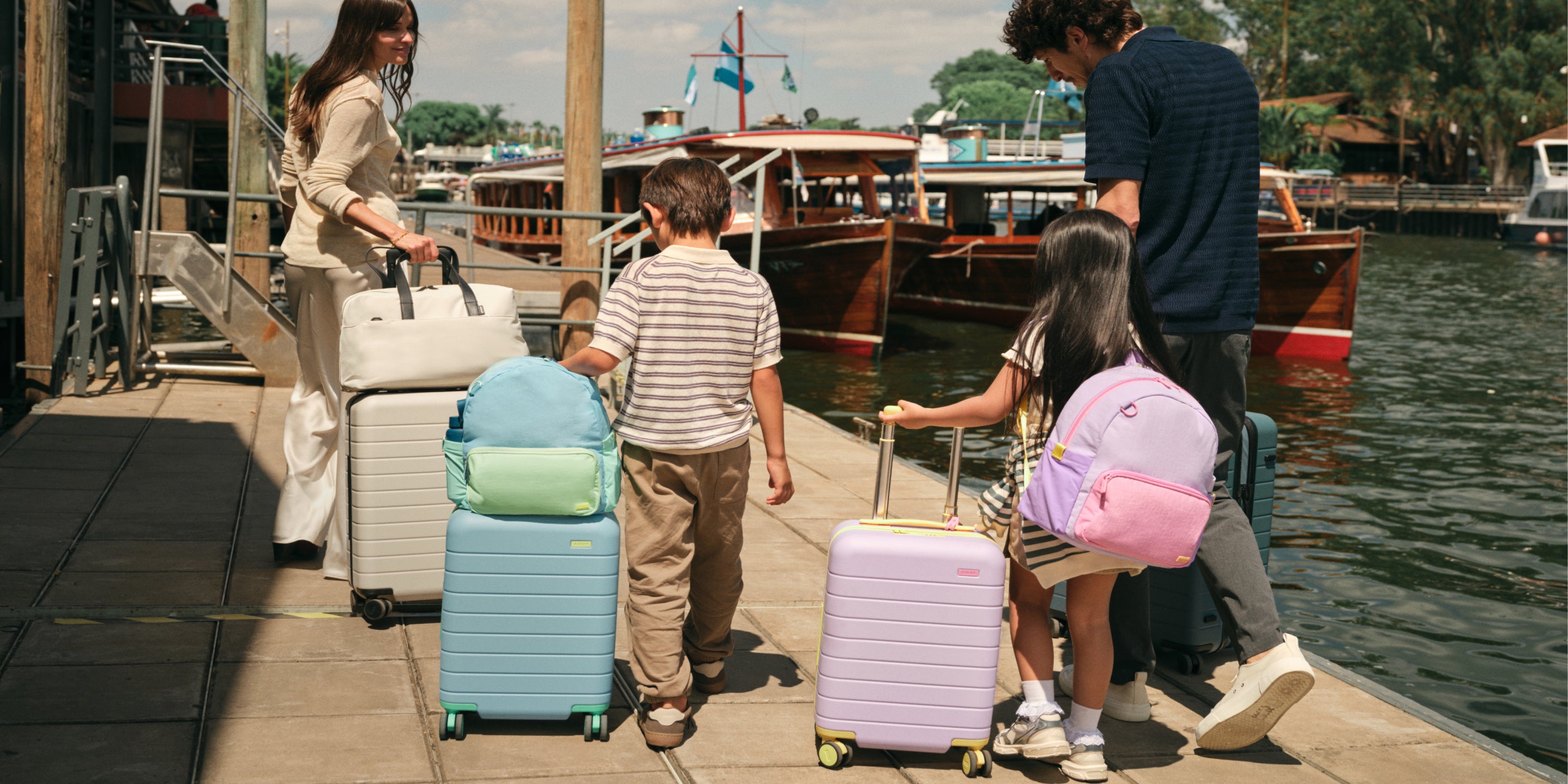 Family with children and suitcases near a dock with boats in the background