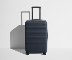 Front product view of The Bigger Carry-On suitcase in Navy Blue with raised handle