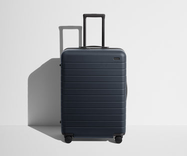 Front product view of The Medium suitcase in Navy Blue with raised handle