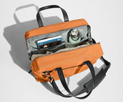 Main compartment packed with a light sweater, notebook, tablet, and water bottle. The detachable shoulder strap is clipped onto the bag.