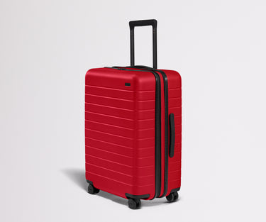 Red suitcase with black handle and wheels on a light gray background