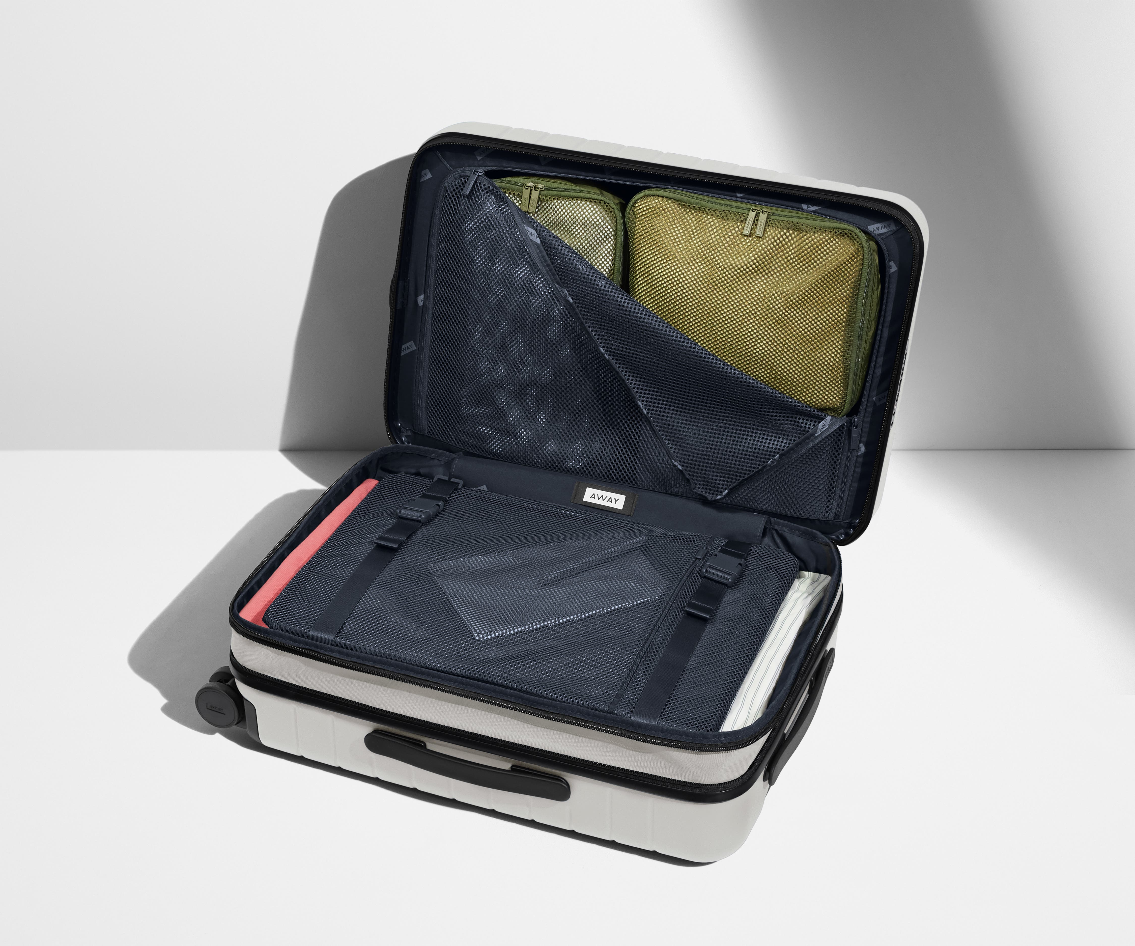 The Bigger Carry-On Flex suitcase in Cloud Gray shown open on its side and packed with Away's packing organizers to show capacity and the interior compression system, designed to help you pack more in