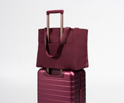 Maroon tote bag on top of a matching maroon suitcase on a light gray background
