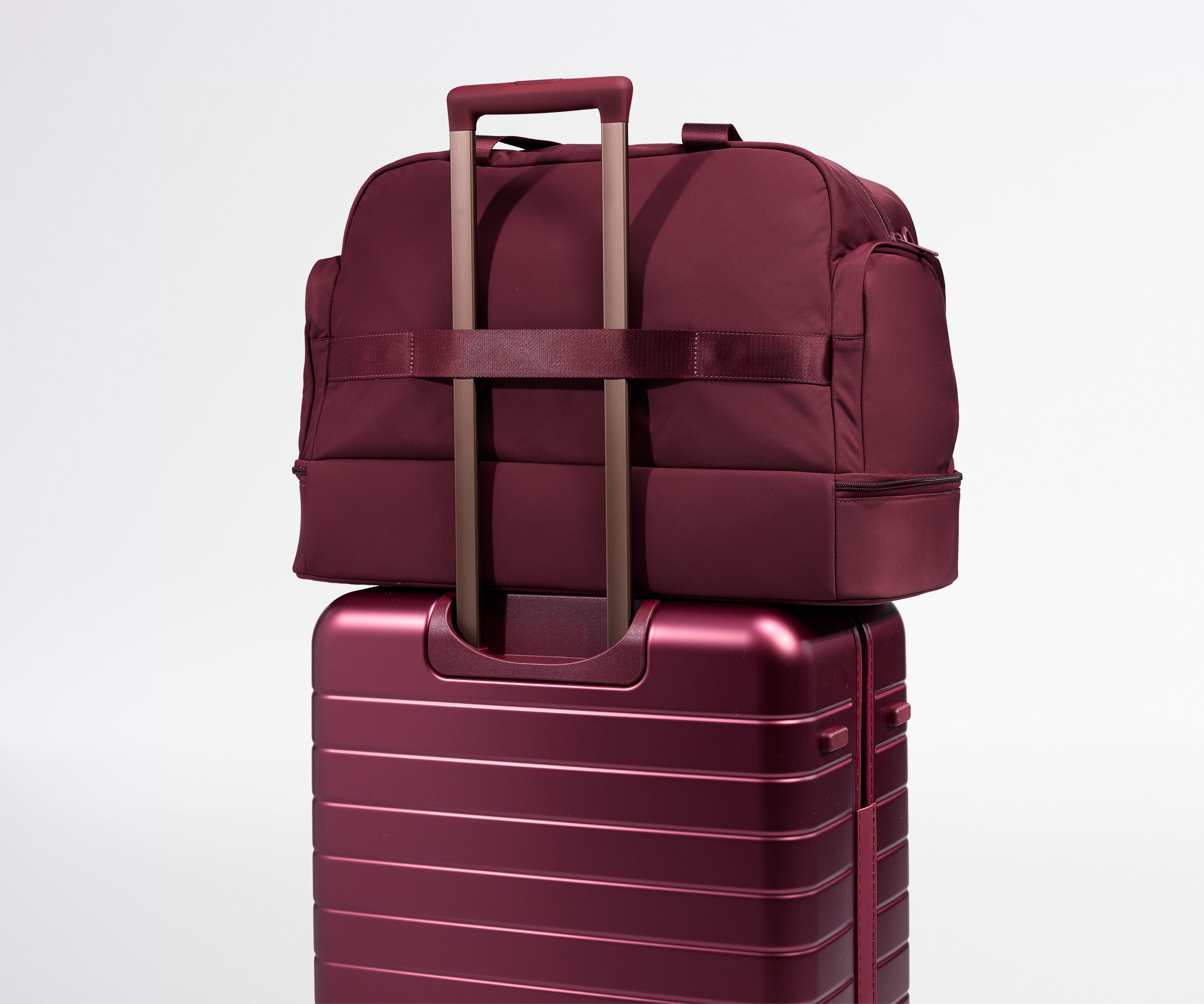 A maroon weekender stacked on a matching suitcase