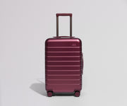 Maroon suitcase with a visible brand logo on a light gray background