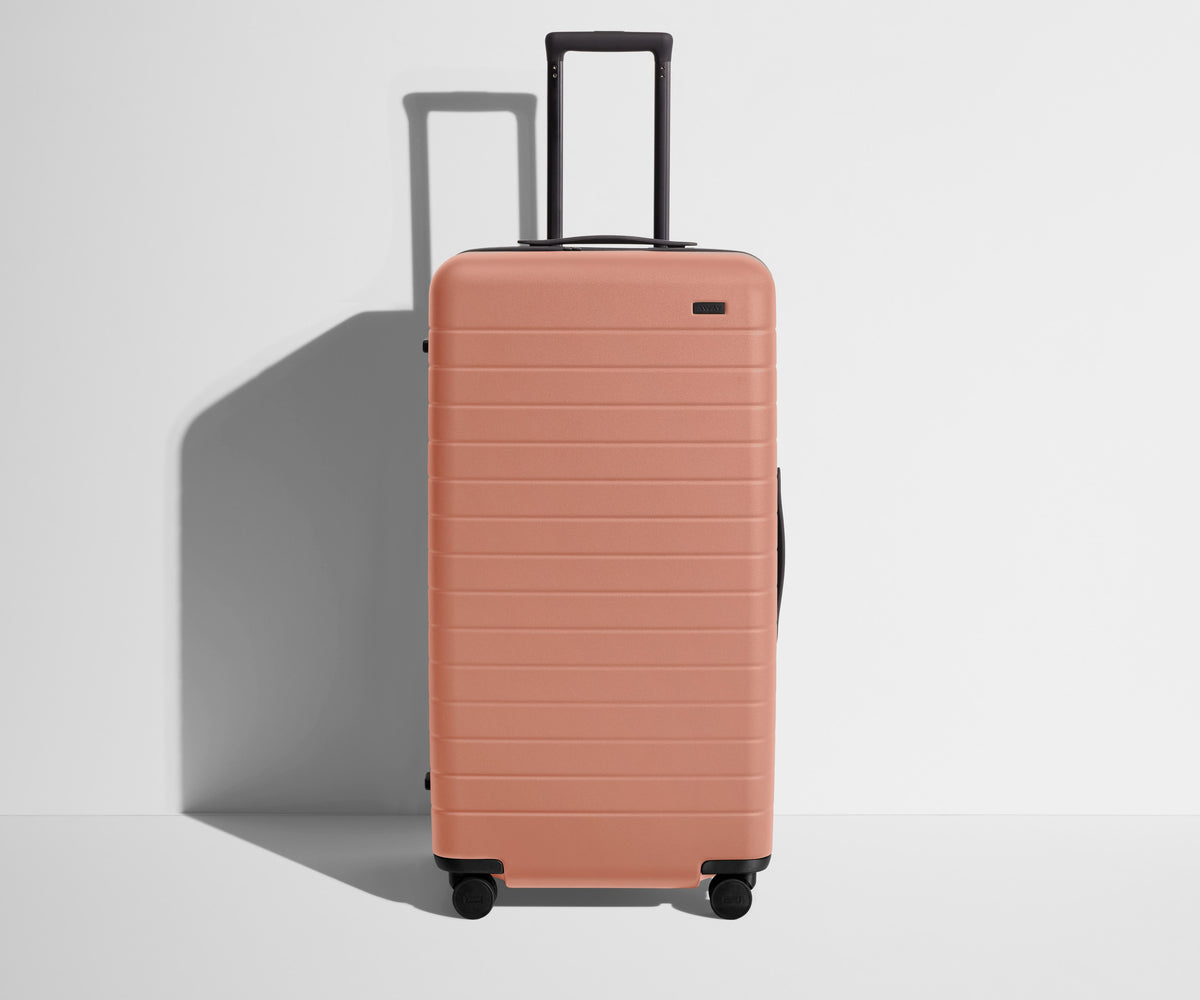 Front product view of The Trunk suitcase in Clay Pink with raised handle