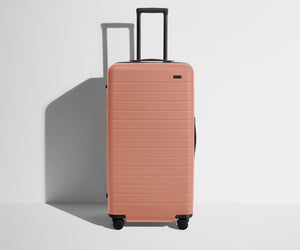 Front product view of The Trunk suitcase in Clay Pink with raised handle