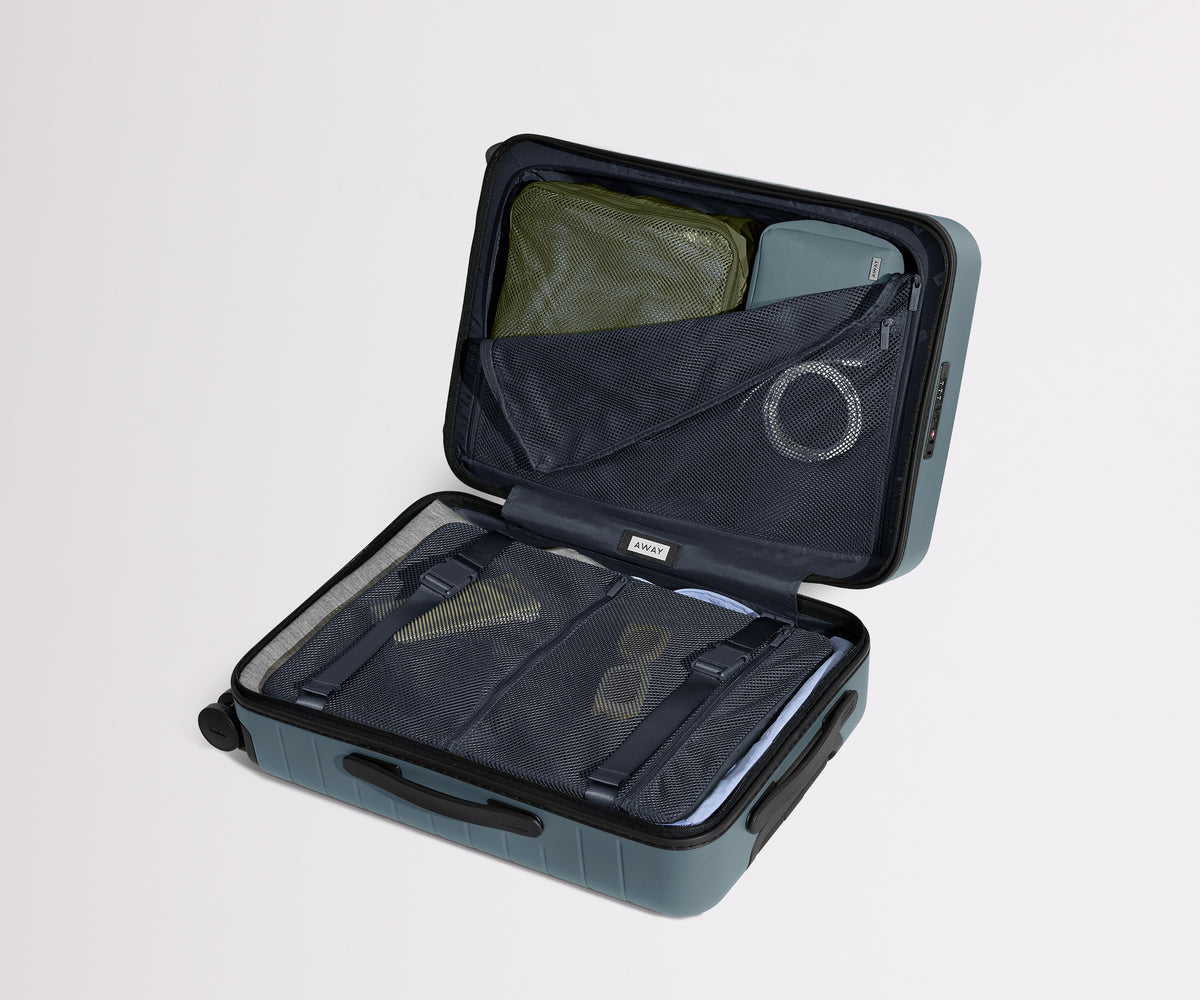 The Bigger Carry-On suitcase in Coast Blue shown open on its side and packed with Away's packing organizers to show capacity and the interior compression system, designed to help you pack more in