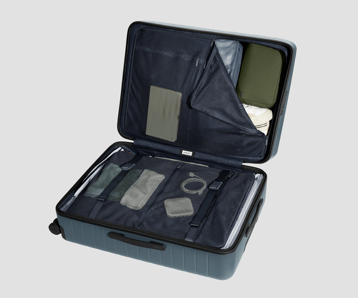 The Large suitcase in Coast Blue shown open on its side and packed with Away's packing organizers to show capacity and the interior compression system, designed to help you pack more in