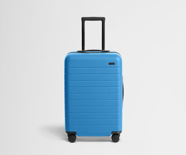 Front product view of The Bigger Carry-On suitcase in Splash Blue with raised handle