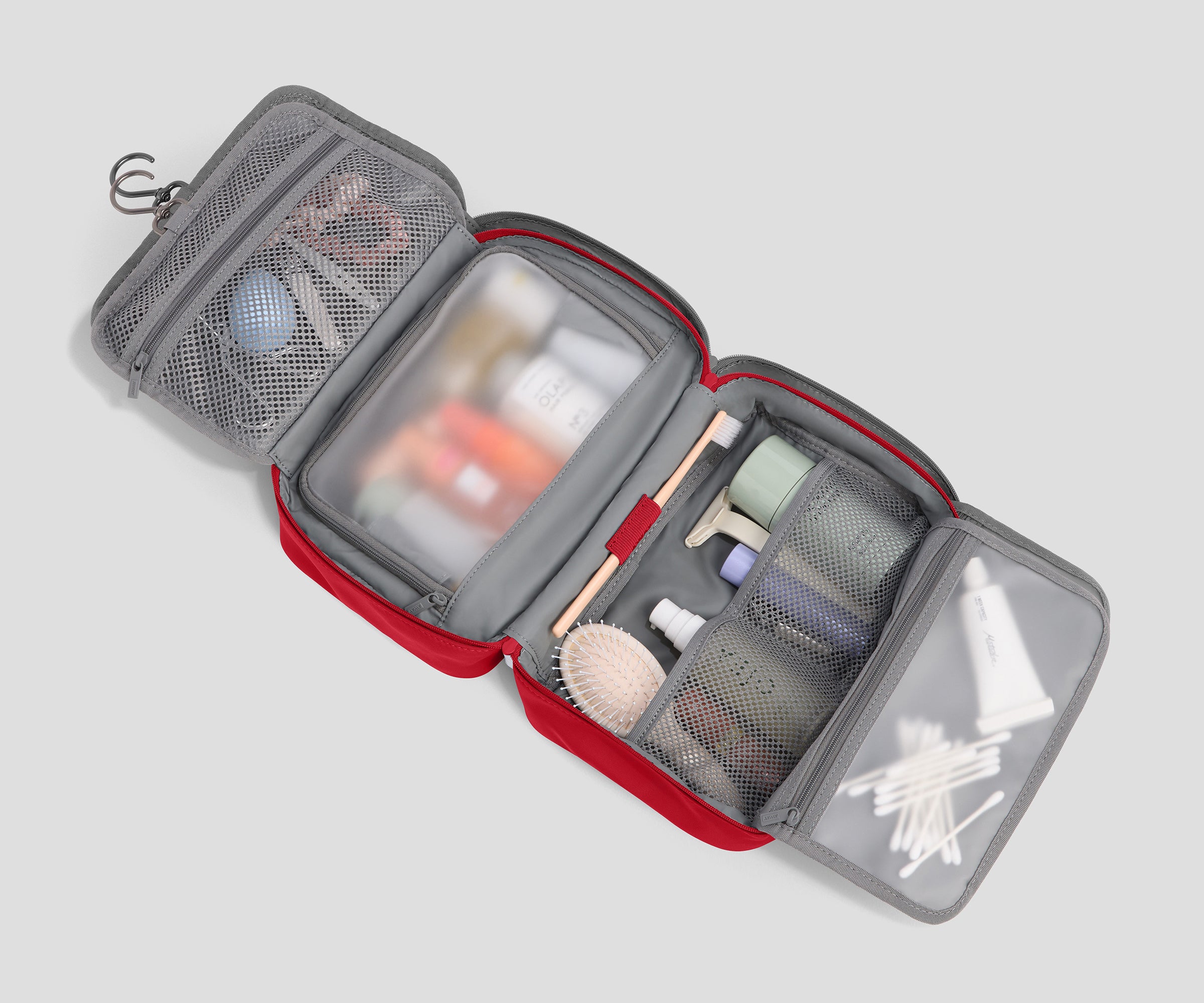 An open gray and red travel toiletry bag with multiple mesh compartments and clear plastic windows, shown against a light gray background.