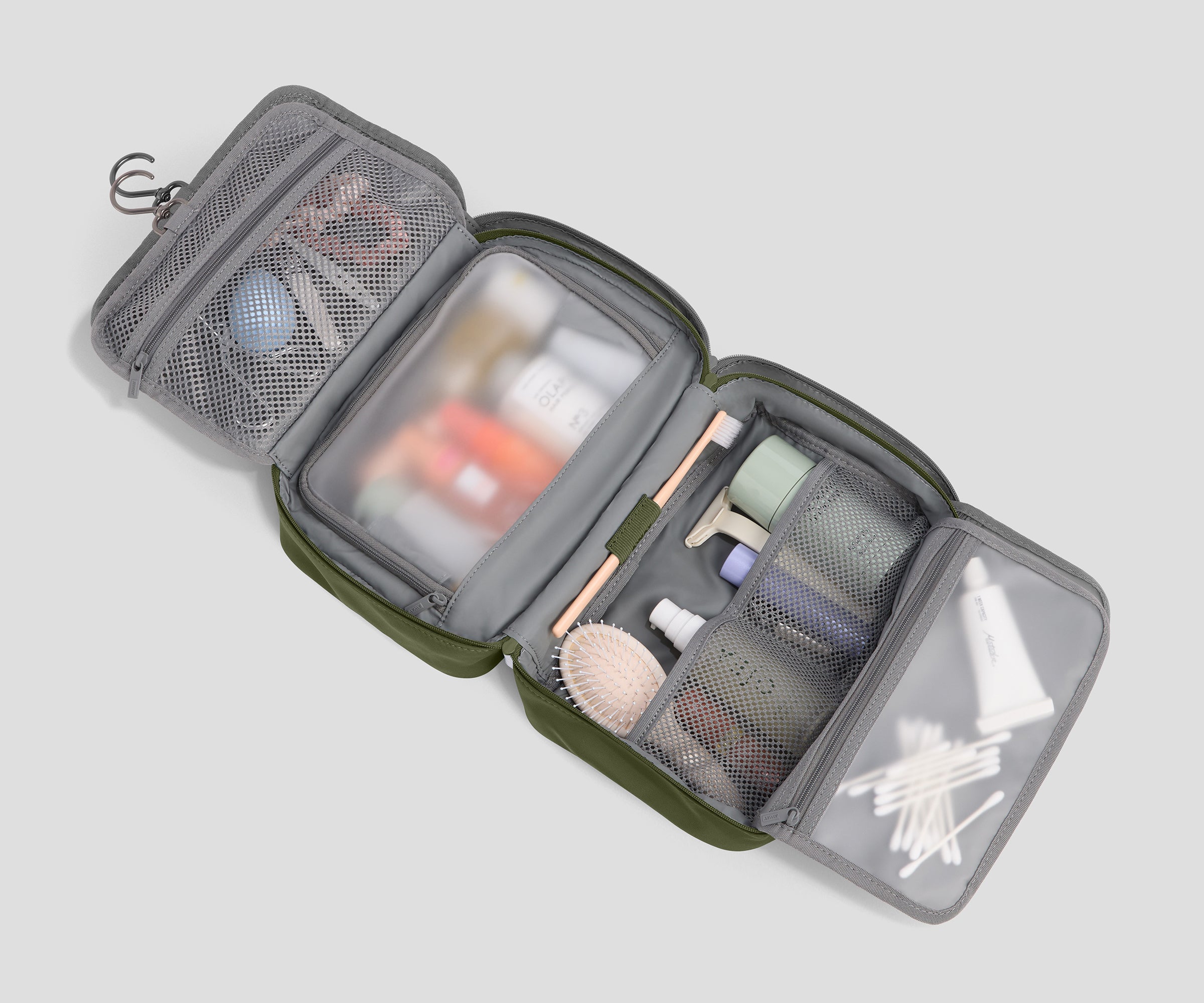 An open green and gray toiletry bag filled with various travel-sized toiletries, shown on a solid light gray background.