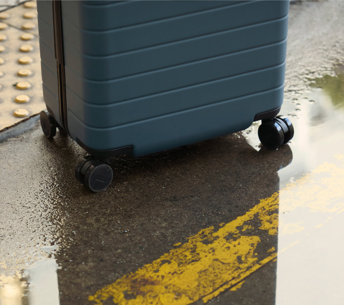 Blue suitcase on wheels on a wet pavement with yellow line