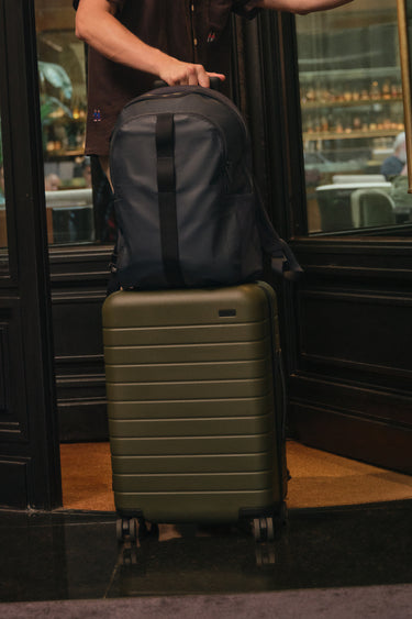 Person holding a backpack on top of a suitcase in a doorway.